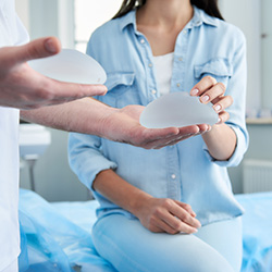 Doctor holding in his hands two silicone implants, female patient trying to touch them