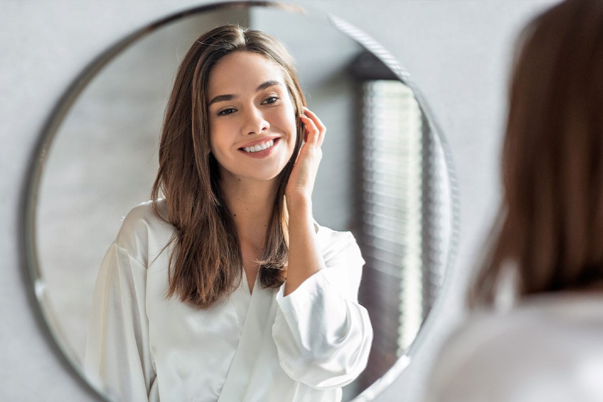 woman looking in the mirror after getting facial fat grafting in Marietta, GA